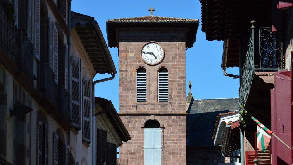 Medieval clock tower in Saint-Jean-Pied-de-Port, France against a clear blue sky.